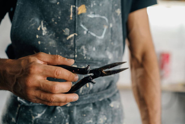 Male artist sculptor artisan works with tongs in workshop - Foto, Bild
