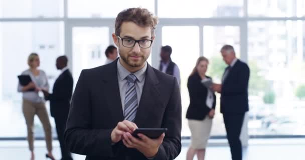 Smiling businessman at a conference working on tablet, reading email messages online with colleagues busy in the background. Face of a smart corporate worker standing and holding wireless technology. - Imágenes, Vídeo