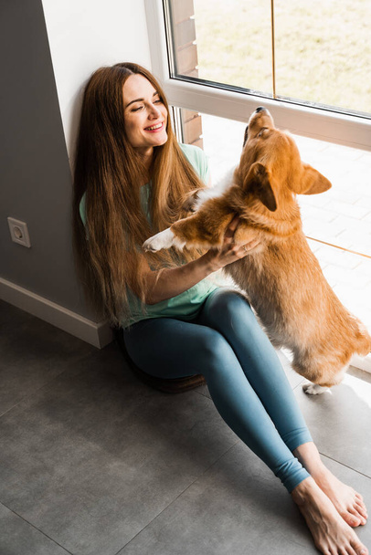 Happy girl hug Corgi dog at home. Lifestyle with domestic pet. Young woman sitting and play with Welsh Corgi Pembroke - Fotó, kép