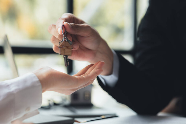 A home rental company employee is handing the house keys to a customer who has agreed to sign a rental contract, explaining the details and terms of the rental. Home and real estate rental ideas. - Zdjęcie, obraz