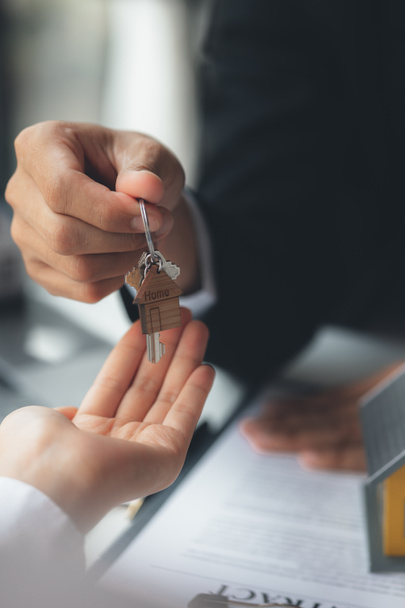 A home rental company employee is handing the house keys to a customer who has agreed to sign a rental contract, explaining the details and terms of the rental. Home and real estate rental ideas. - Фото, изображение
