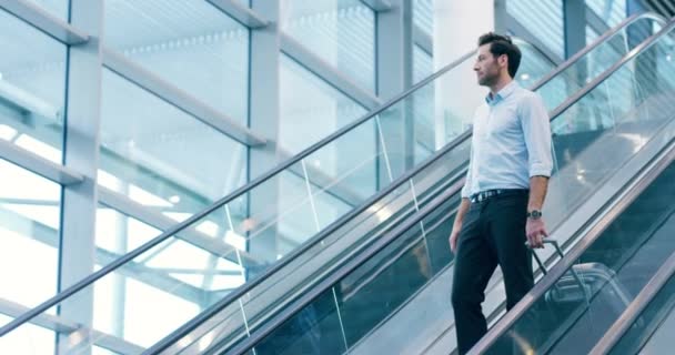 A traveling professional business man at the airport, holding a suitcase and taking a trip to a new city. A corporate executive coming down an escalator with luggage in hand on his way to a new town - Metraje, vídeo