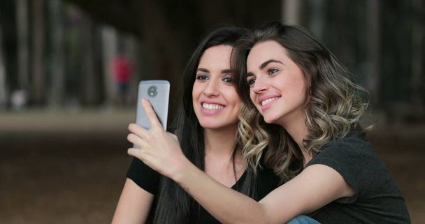 Friends together outside holding cellphone taking selfie at the park - Foto, afbeelding