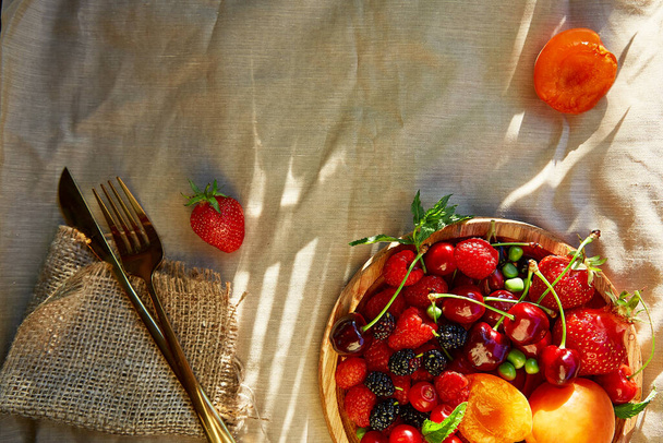 Summer fruits and berries seasonal background under hard shadows. Strawberries, apricots, cherry, raspberry with cutlery. Healthy snack, natural dessert, vitamins. Copy space - Photo, Image