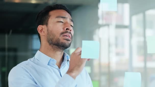 Professional man brainstorming and planning, thinking of marketing ideas while writing on sticky notes at work. Focused male making a visual board while researching a strategy and managing his tasks. - Materiaali, video