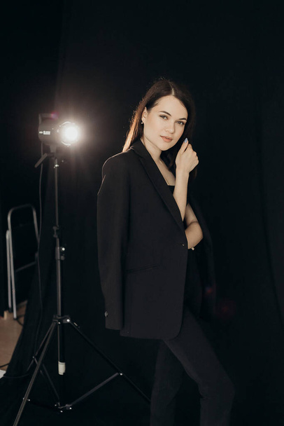 A girl in a black suit stands on a black background - Fotoğraf, Görsel