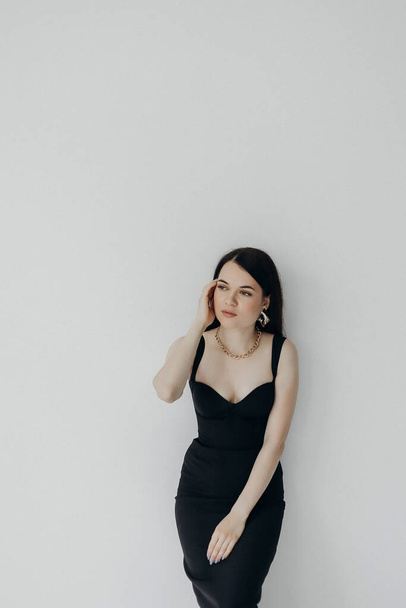 A girl in a black dress stands on a white background - Φωτογραφία, εικόνα