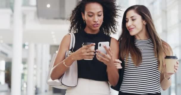 Female friends and girlfriends chatting, laughing and walking together while having coffee. Smiling women talk about business news and working life. Young ladies looking at social media on a phone. - Filmagem, Vídeo