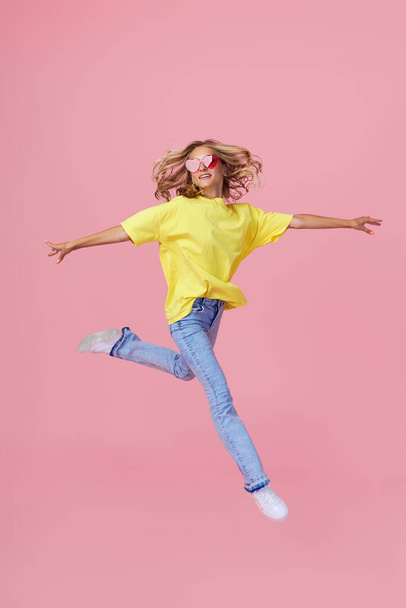 Full length portrait of a joyful young woman in casual clothes jumping and celebrating on a pink background - Foto, immagini