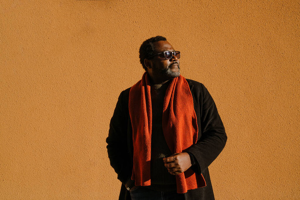 Black bearded man in sunglasses standing by wall outdoors - Фото, изображение