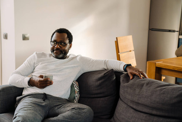 Black man using mobile phone while watching tv on sofa at home - Фото, зображення