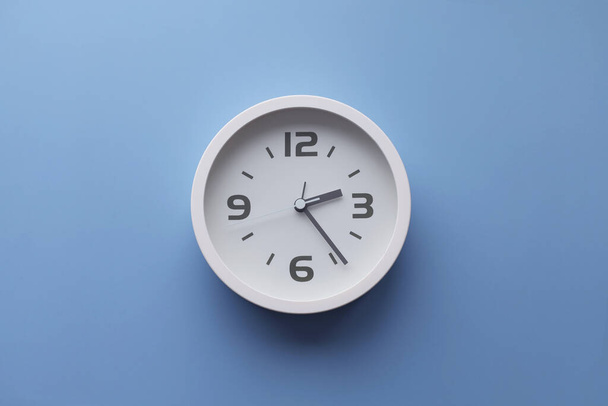 White wall clock on the wall. Minimalist flat lay image of plastic wall clock over blue turquiose background with copy space and central composition. - Φωτογραφία, εικόνα