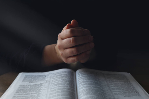 Kobieta ręce na Biblii. ona jest czytanie i modlitwę nad Biblią w ciemne miejsce na drewnianym stole. - Zdjęcie, obraz