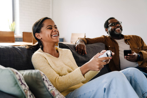 Black girl playing on video game while her father using cellphone at home - Фото, зображення