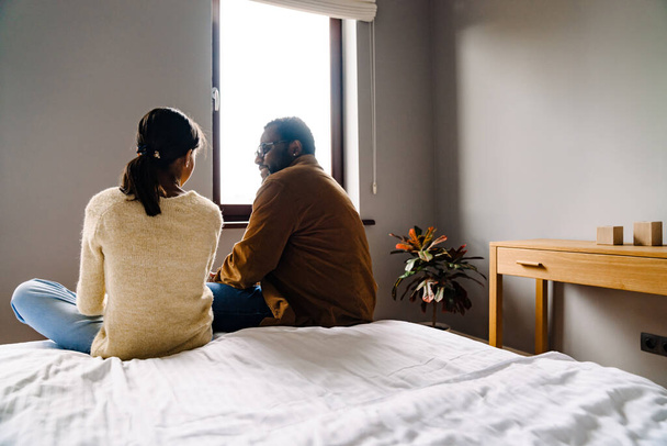 Black girl and her father talking while sitting on bed at home - Photo, image