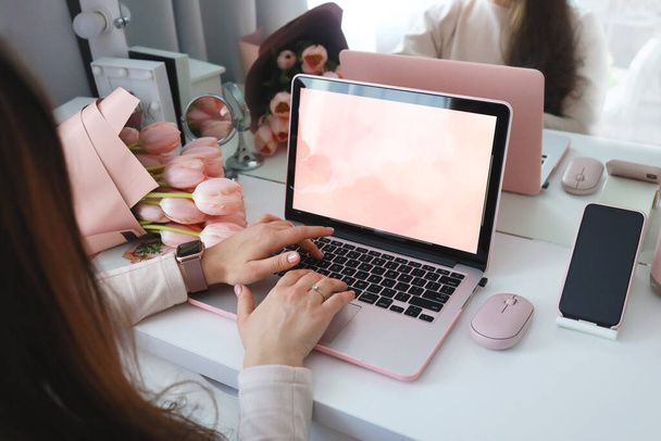 Female hands using laptop. Female office desk workspace homeoffice mock up with laptop, pink tulip flowers bouquet, smartphone and pink accessories. - Foto, afbeelding