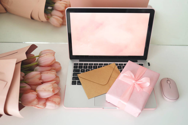 Styled feminine desk workspace with pink tulips, laptop computer and envelope. Top view notebook screen. Pink gift box and pink computer mouse. - Fotoğraf, Görsel