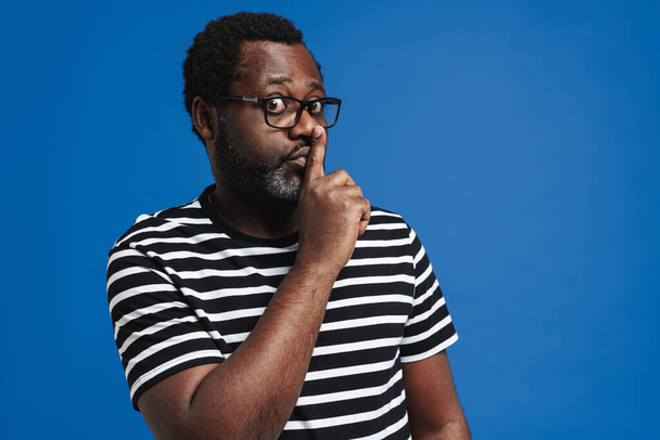 Black surprised man showing silence gesture at camera isolated over blue background - Fotó, kép