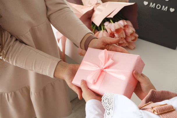 Child's hands hold beautiful pink gift box with ribbon. Pink tulip flower and sign i love you mom in background. Top view, close-up. Preparing for the holidays. - 写真・画像