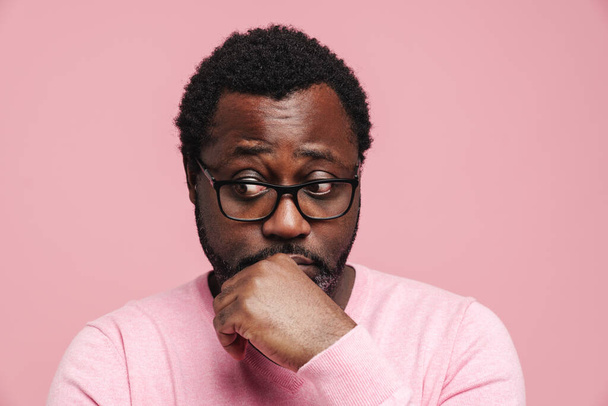 Black puzzled man in eyeglasses posing and looking aside isolated over pink background - Foto, immagini