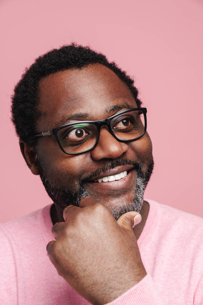 Black bearded man in eyeglasses smiling and looking at camera isolated over pink background - Foto, Imagen