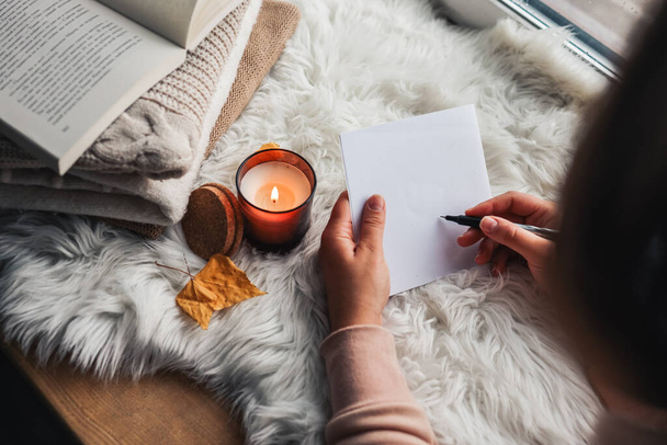 The girl writes a letter on the background of a candle. Home comfort. - Fotoğraf, Görsel