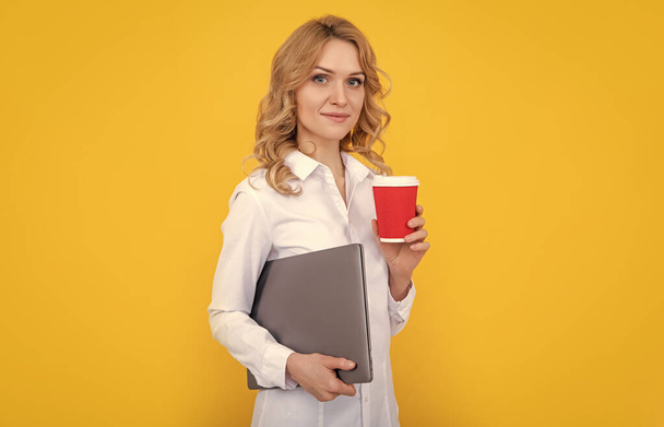 Sarı arka planda kahve fincanı ve dizüstü bilgisayarla gülümseyen sarışın kadın.. - Fotoğraf, Görsel
