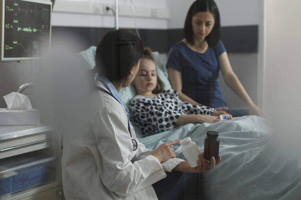 Doctor expert recommending antibiotics for ill kid sickness hospitalized in children healthcare facility. Expert pediatrician prescribing medication for little girl disease resting in patient bed. - Foto, afbeelding