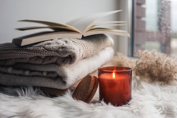 Burning candle and sweaters with a book on the windowsill. Autumn mood. - Foto, Imagem