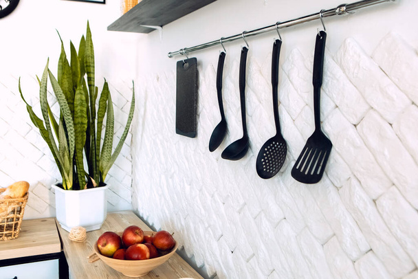 Close up kitchen supplies equipment, houseplant on the wooden table with kitchenware. Set of utensils hanging on the wall. Modern interior, different devices - Photo, image