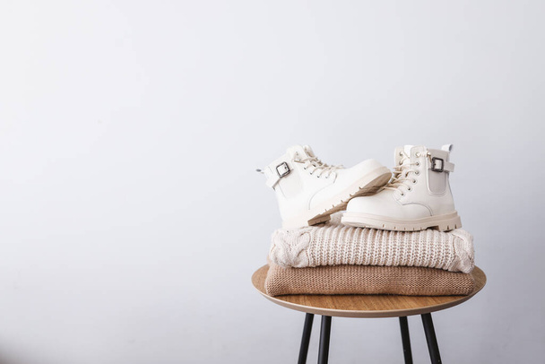 Stack of sweaters and boots on a wooden table. Place for text. Advertising. - Photo, image