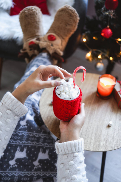 A girl holds a cup of cocoa with marshmallows and candy in her hands. Cozy New Year's mood. - Foto, imagen