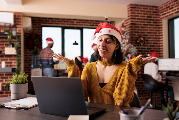 Business woman talking on videocall conference in office with christmas tree and festive decorations. Attending remote teleconference call and online meeting during holiday season at work. - 写真・画像