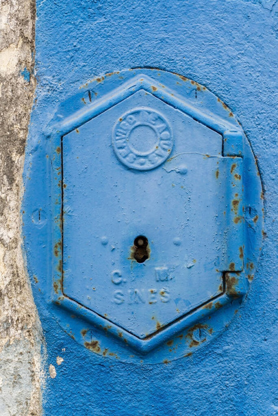 Old rusty blue painted iron lid of a valve box of the SERVICO DE AGUA PUBLIC WATER SUPPLY on the chipped white - blue painted wall of a house in the Old Town area, Portugal - Φωτογραφία, εικόνα