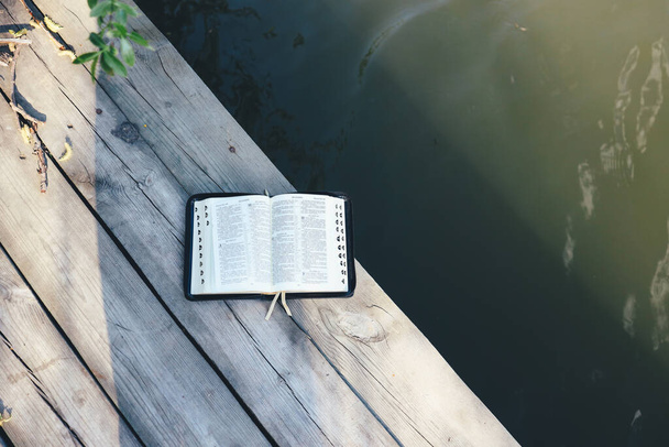 Open Bible on a wooden board near the river, top view, space for your text - Foto, Bild