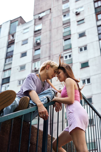 A lovely teenage couple is hugging and snuggling outside in an urban exterior surrounded by buildings and skyscrapers. - Zdjęcie, obraz