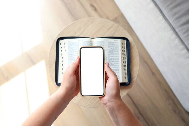 Woman hand hold and touch screen smart phone,cellphone in church over blurred bible holy and age book. - Foto, afbeelding