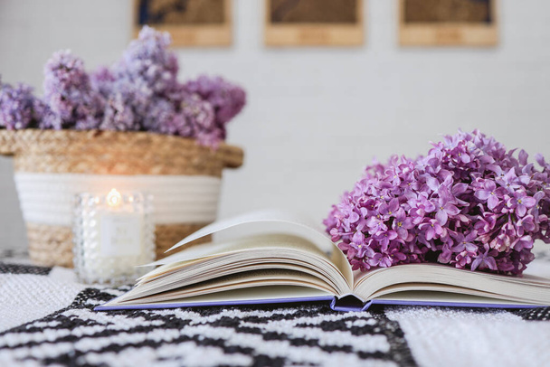 Wicker basket with lilacs, a candle, an open book on the table.Good morning concept. - Valokuva, kuva