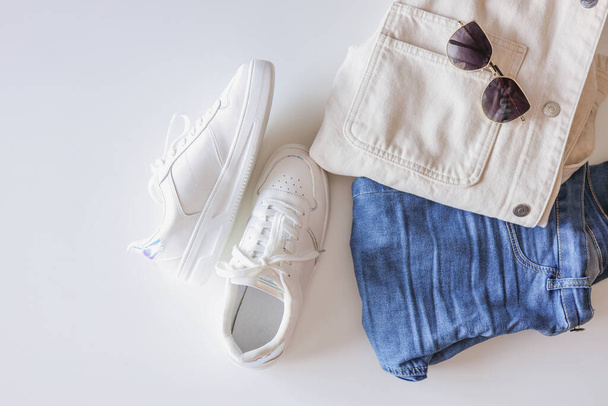 Stylish women's clothing flat lay. White sneakers, jeans and a jacket on a white background top view. - Foto, Imagen