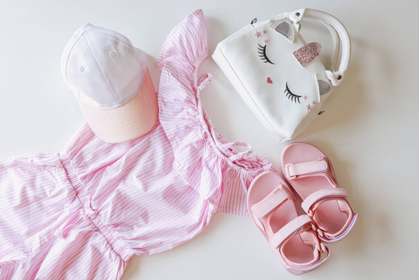 Set of children's clothes for girls in pink style. Sandals, cap and t-shirt, flat lay, top view. - Fotó, kép