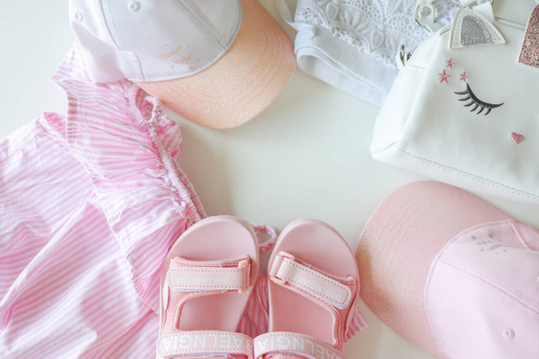 Set of children's clothes for girls in pink style. Sandals, cap and t-shirt, flat lay, top view. - Photo, Image
