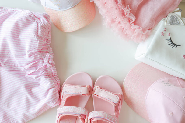 Set of children's clothes for girls in pink style. Sandals, cap and t-shirt, flat lay, top view. - Foto, Imagen