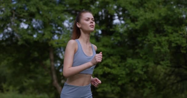 Mulher em uma corrida de manhã no parque em um traje de treino contra um fundo de árvores. Imagens 4k de alta qualidade - Filmagem, Vídeo