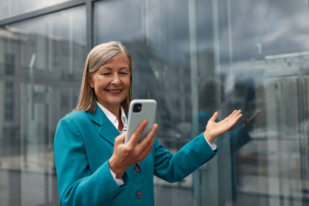 Senior Woman Gesturing, Chatting Video Call Using Smartphone on City Street. Confident Smiling Beautiful Female using Mobile Phone Alone. Corporate Lifestyle Concept - Foto, Imagen