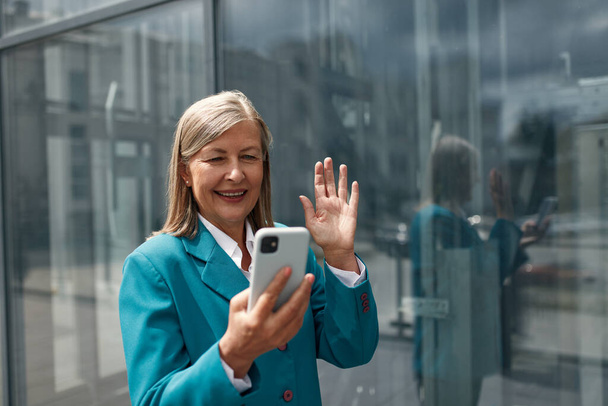 Beautiful Senior Woman Standing, Using Smartphone on City Street. Confident Smiling Beautiful Female using Mobile Phone for Video Call. Corporate Lifestyle Concept - Photo, image