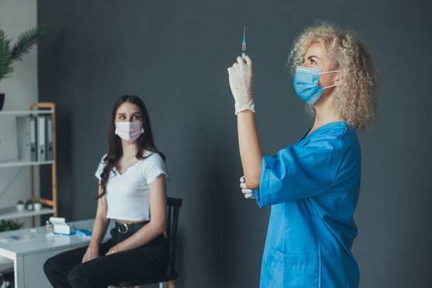 Curly-haired nurse preparing coronavirus vaccine for woman patient at vaccination center. Coronavirus immunization flu treatment vaccination. Covid 19 and - Φωτογραφία, εικόνα