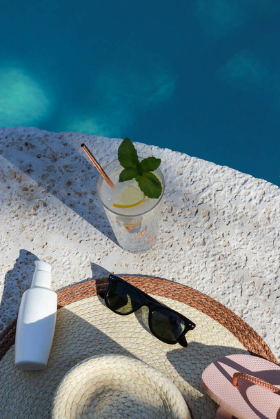 a glass of water with lemon, summer hat and sunglasses at the pool - Photo, image