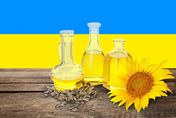 Bottles of sunflower oil and seeds on wooden table against flag of Ukraine - Photo, Image