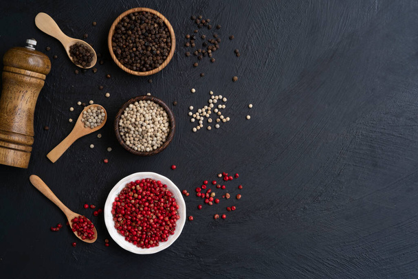 black white and red peppercorns in the wooden bowl before mix decoration with the wooden spoon and pepper grinder, mix chilli pepper top view on a dark kitchen table background with copy space - 写真・画像
