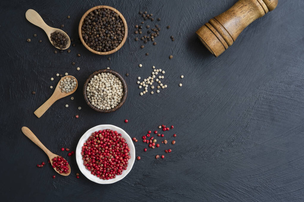 black white and red peppercorns in the wooden bowl before mix decoration with the wooden spoon and pepper grinder, mix chilli pepper top view on a dark kitchen table background with copy space - 写真・画像